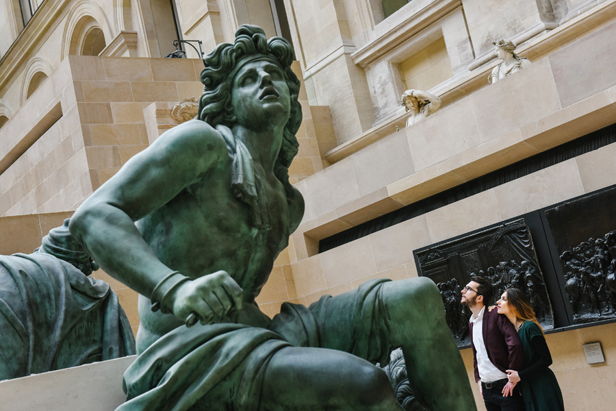 une femme et un homme regardent une sculpture dans le musée du Louvre