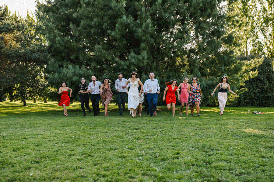 les mariés et leurs amies courent dans un jardin vers le photographe