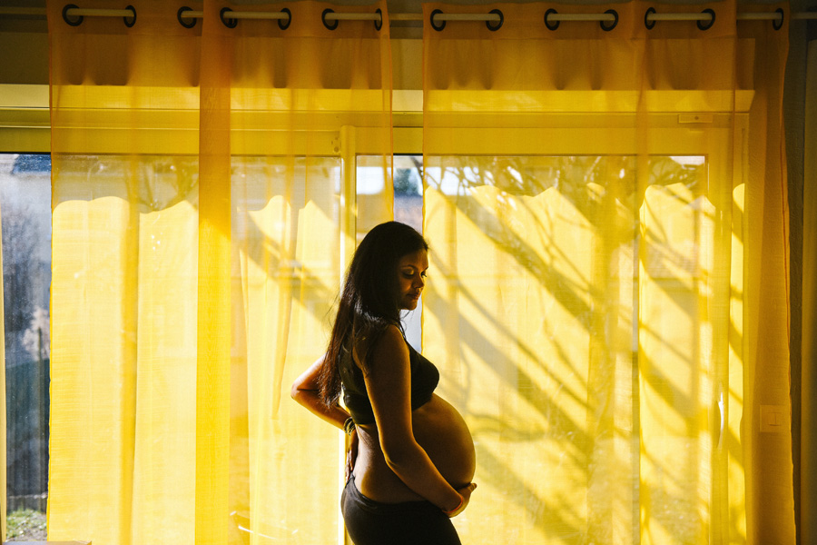 une femme enceinte pose devant un rideau jaune
