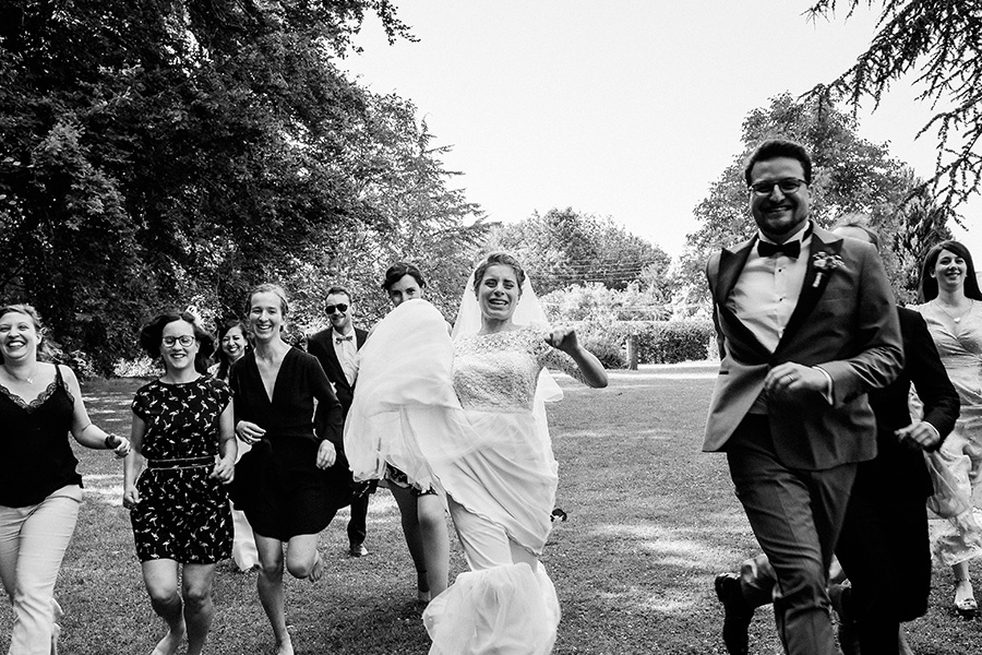 les mariés et leurs amis courent vers le photographe pendant une photo de groupe