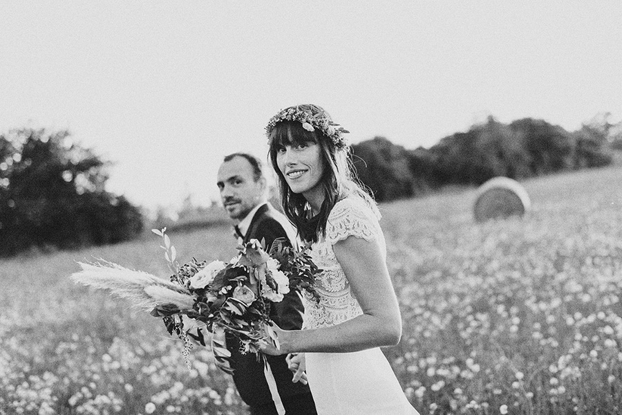 les mariés marchent dans un champ pendant leur séance photo