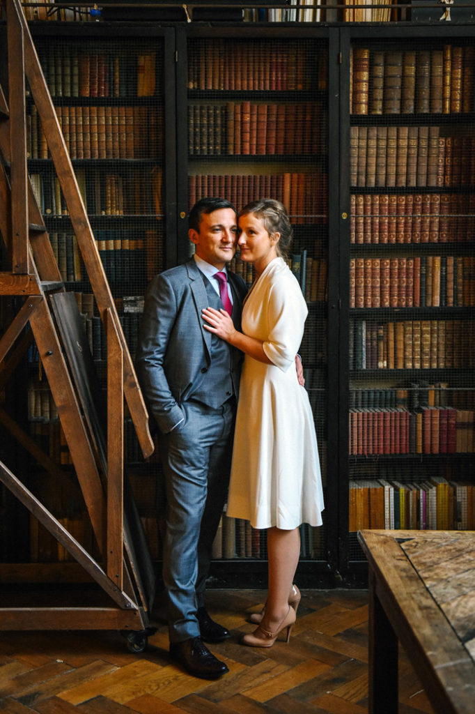 Un couple de jeunes mariés pose devant une bibliothèque