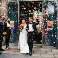 Un couple célèbre son mariage en petit comité en sortant de la mairie sous une pluie de confettis, entouré de leurs proches.