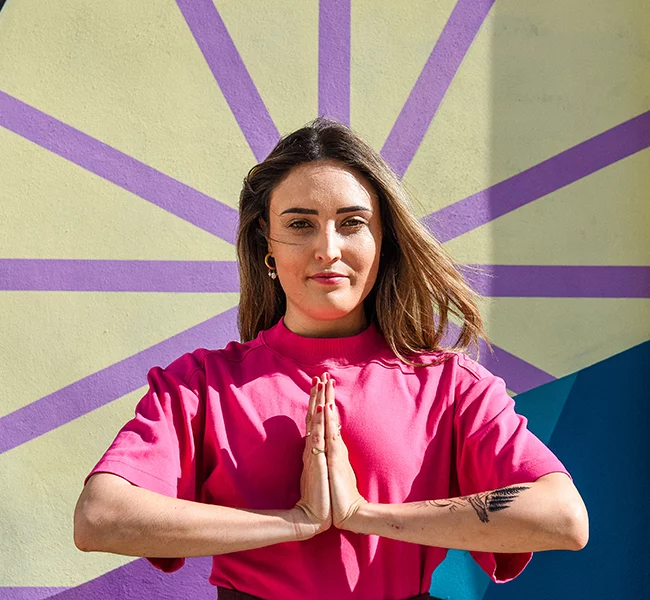 Une femme joint les mains devant une fresque colorée