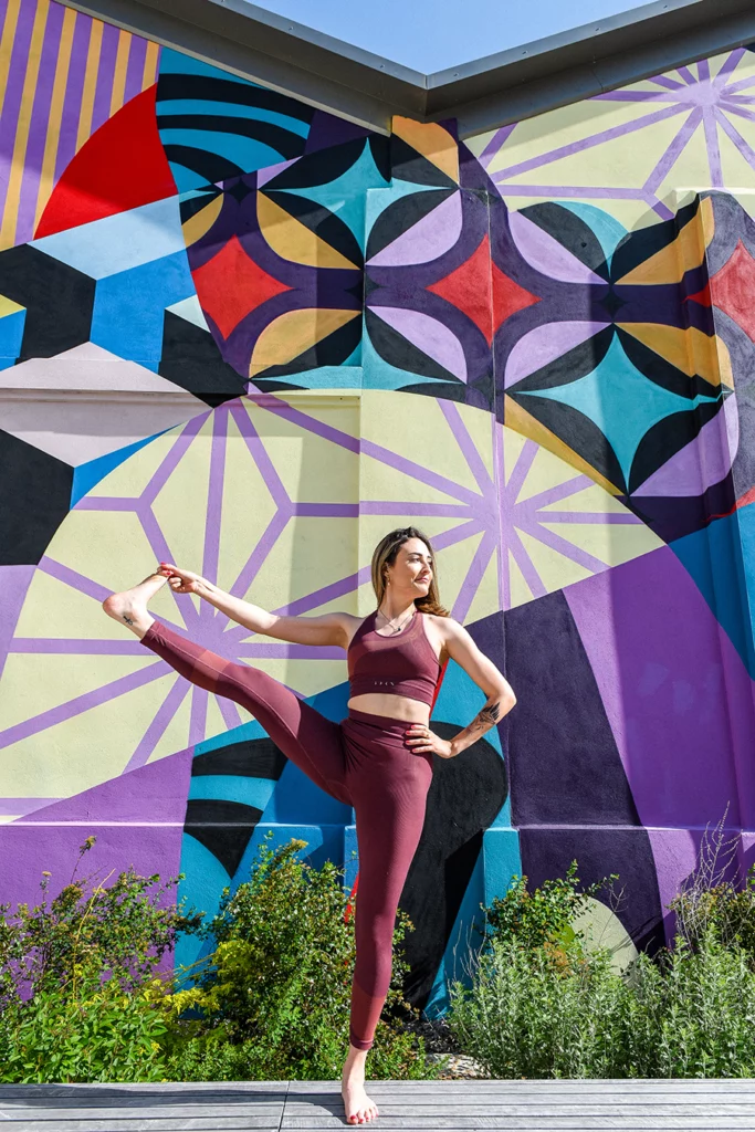 Une femme pose devant une fresque colorée en ville.