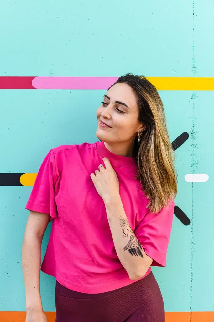 Une jeune femme pose devant un mur en couleurs et sourit.
