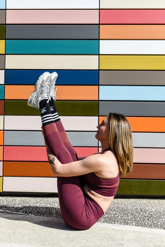 Une femme fait une pose de yoga devant un mur coloré